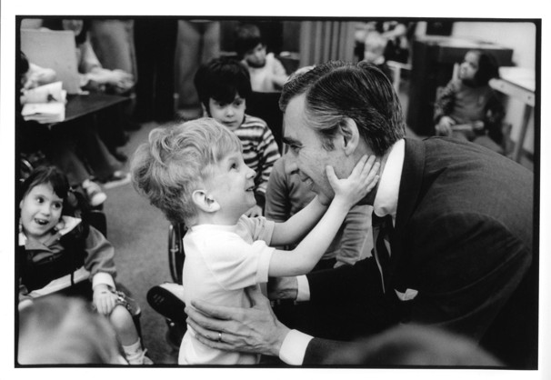 A little boy grinning and grasping Mr. Rogers's face