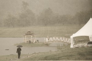 Man with an umbrella walks toward a wedding tent in pouring rain