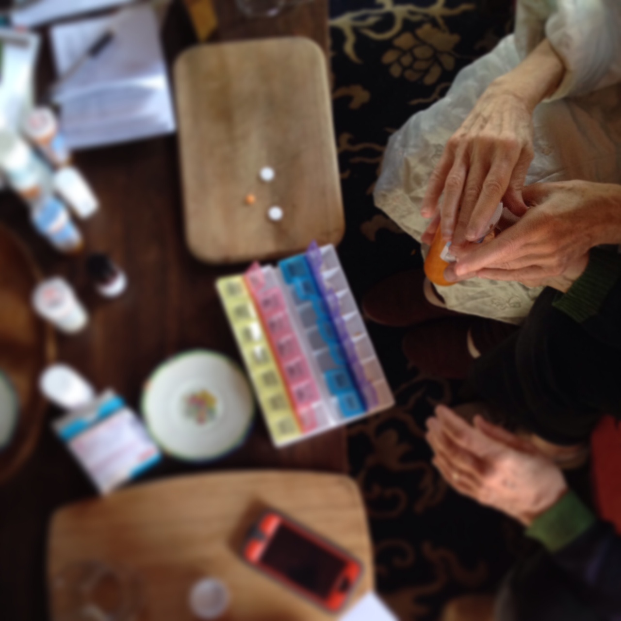 Two sets of hands sort pills into a pillbox