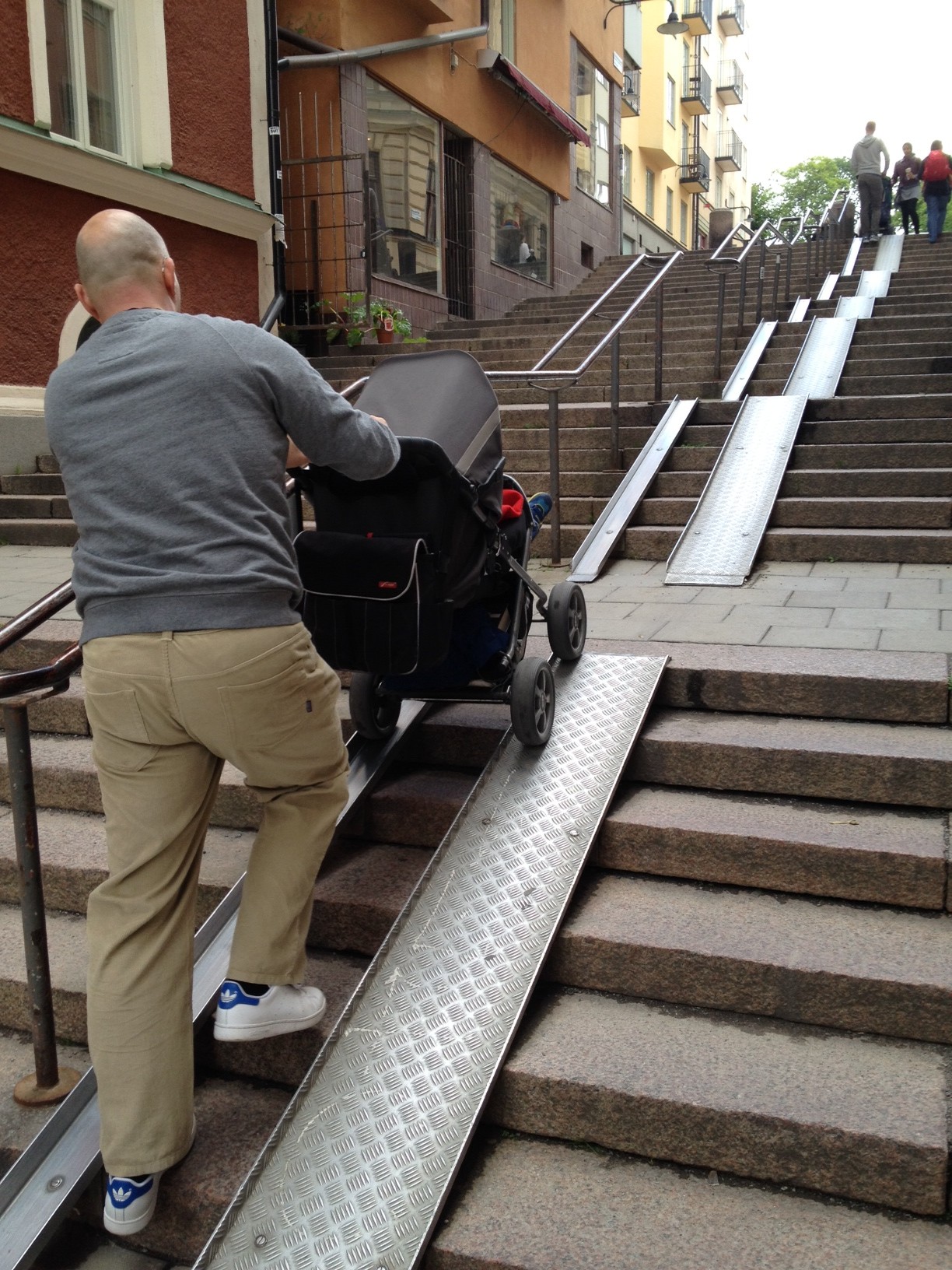 Man pushes stroller up tracks covering stairs in Stockholm