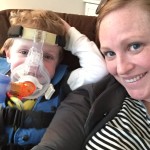 Boy wearing nebulizer mask and his mom