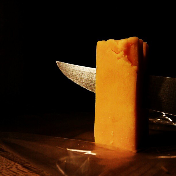 cheddar cheese being sliced by a sharp knife