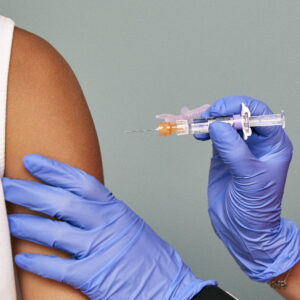 Gloved hands administering a shot to an arm