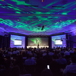 Green and purple kaleidoscopic lights on the ceiling of a stage in front of a large audience